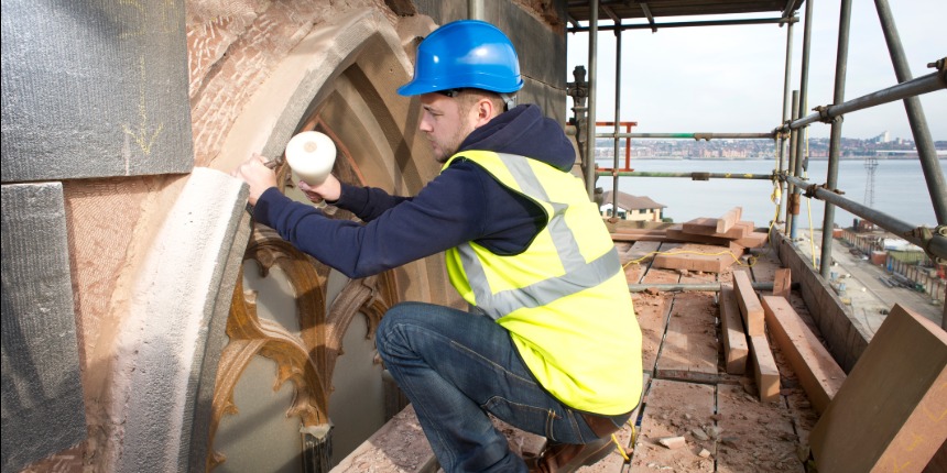 Stonemason in hi-vis jacket, crouched down working on a church restoration