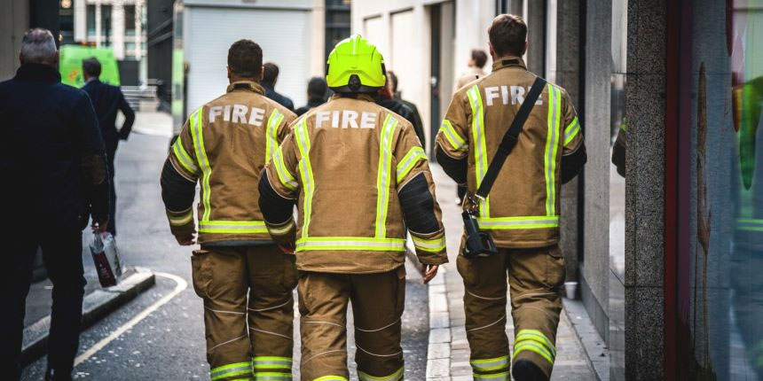 Three fire fighters walking with their backs to the camera through the streets of London.