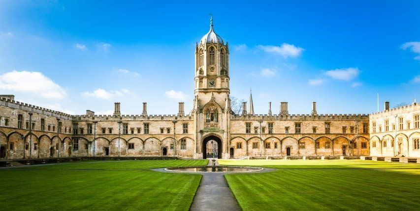 A photograph of Oxford University including lawns and fountain on a sunny day with blue skies. 
