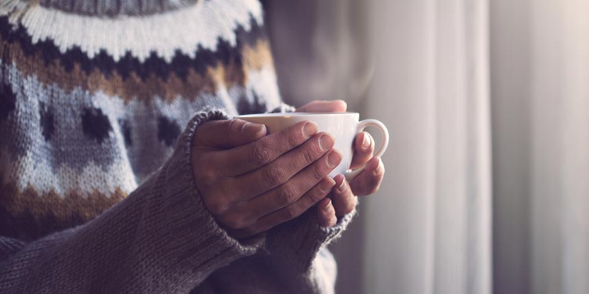 Someone wearing a winter jumper holding a hot drink